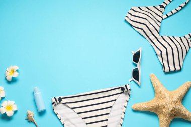 Açık mavi arka planda güzel mayosu, çiçekleri ve deniz yıldızıyla bezenmiş düz bir kompozisyon. Metin için boşluk