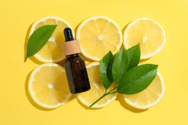 Sarı arka planda bir şişe temel yağ, limon ve yeşil yaprak, düzlük.