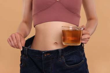 Kilo verme konsepti. Bir fincan diyet çayı ve bej arka planda büyük pantolonu olan kadın, yakın plan.