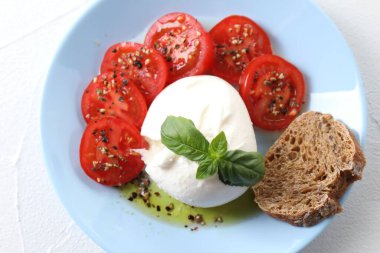 Lezzetli burrata peyniri, domates, fesleğen ve ekmek beyaz masada.