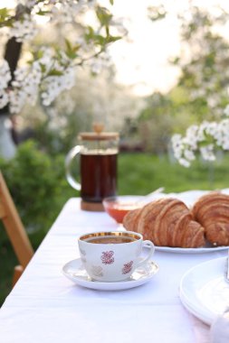 Baharın bahçesinde çay ve kruvasanlarla süslü bir masa.