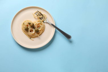 Açık mavi arka planda lezzetli spagetti, çatal, zeytin ve peynirden yapılmış bir kalp. Metin için boşluk