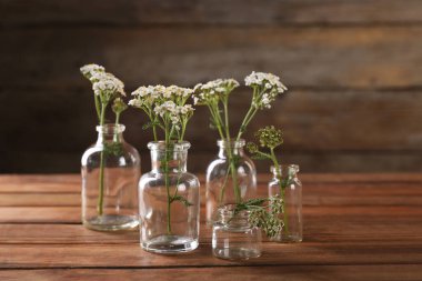 Ahşap masanın üzerinde cam şişelerde yarrow çiçekleri.