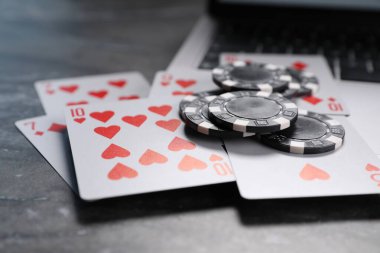 Poker fişleri, dizüstü bilgisayar ve kart oyunları gri masada, yakın plan. Çevrimiçi oyun