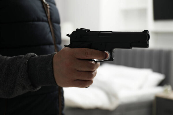 Dangerous criminal with gun in foreign house, closeup. Armed robbery