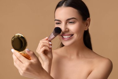 Kozmetik ürünüyle gülümseyen kadın bej arka plana makyaj yapıyor.