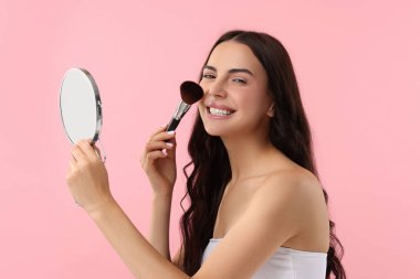 Gülümseyen kadın pembe arka planda makyaj yapıyor.