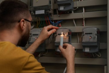 Mumlu adam içeride elektrik sayacını kontrol ediyor.