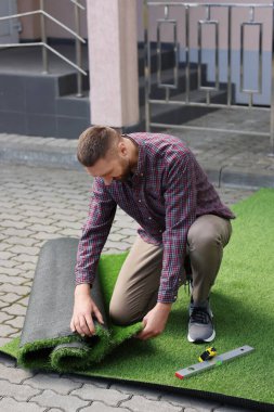 Genç adam dışarıda yapay yeşil çim kuruyor.