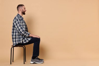 İyi duruşu olan bir adam soluk turuncu arka planda sandalyede oturuyor, mesaj için yer var.