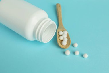 Homeopati. Açık mavi arka planda haplı şişe ve kepçe