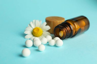 Homeopati. Haplı bir şişe ve açık mavi arka planda papatya çiçeği, yakın plan.