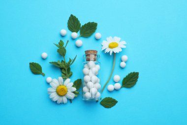 Homeopati. Cam şişe, haplar, papatyalar ve açık mavi arka planda yeşil yapraklar, düz uzanma