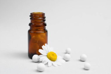 Homeopati. Cam şişe, haplar ve beyaz arka planda papatya çayı.