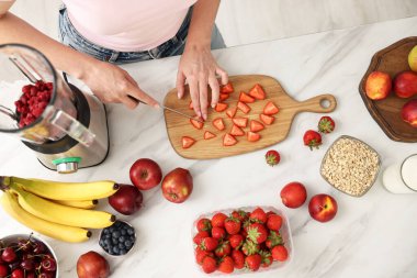 Kadın mutfaktaki beyaz mermer masada blender ile nefis smoothie yapıyor.