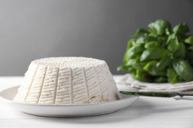 Lezzetli ricotta (krem peynir), beyaz ahşap masada bıçak ve fesleğen, yakın plan.
