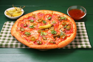 Lezzetli pizza Diablo, sos ve yeşil ahşap masada salamura biber.