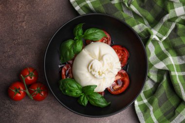 Lezzetli burrata peyniri, domates ve fesleğen kahverengi masada.