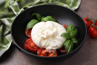 Lezzetli burrata peyniri, domates ve fesleğen kahverengi masada, yakın plan.