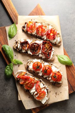 Lezzetli ricotta bruschettalar, güneşte kurutulmuş domates, sos ve fesleğen, gri desenli masa, üst manzara.