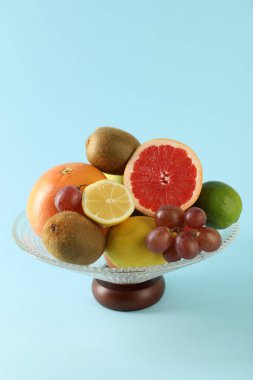Açık mavi zemin üzerinde farklı taze meyveler bulunan cam vazo.