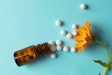 Homeopati. İçinde haplar ve açık mavi arka planda çiçek olan bir şişe.