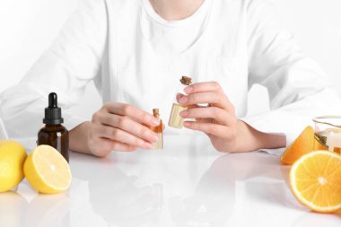 Aromaterapi ürünü. Bilim adamı laboratuarda, yakın planda, beyaz masada gerekli yağları geliştiriyor.