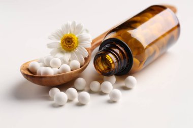 Homeopatik tedavi. Beyaz arka planda haplı kaşık, şişe ve papatya çiçeği.
