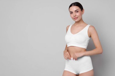 Diyet ve kilo verme konsepti. Açık gri arka planda zayıf vücutlu güzel bir genç kadın. Metin için boşluk