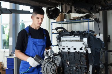 Genç oto tamircisi otomobil tamirhanesinde motor tamir ediyor. Araç tanılayıcı