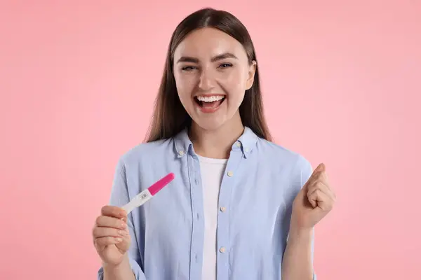 stock image Happy woman holding pregnancy test on pink background