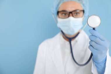 Açık mavi arka planda steteskop tutan doktor, seçici odak