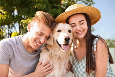 Happy couple with cute Golden Retriever dog outdoors on sunny day