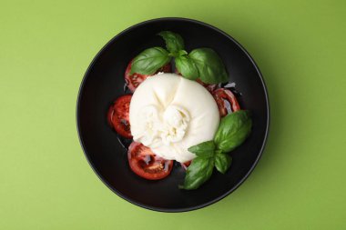 Lezzetli burrata peyniri, domates ve fesleğen yeşil masada, üst tarafta.