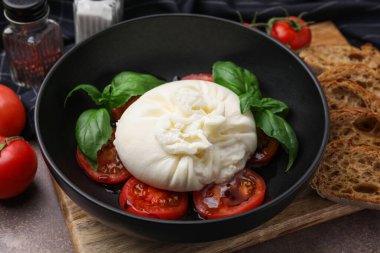 Lezzetli burrata peyniri, domates ve fesleğen kahverengi masada, yakın plan.