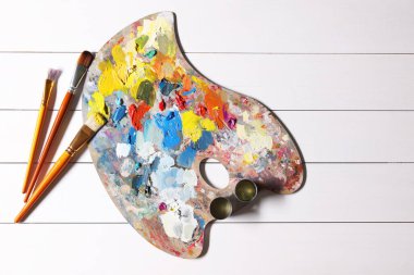 Sanatçı paleti, fırçalar, beyaz ahşap masa boyaları, düz yatak. Metin için boşluk