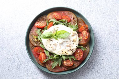 Açık gri desenli masada, kasede taze burrata salatası.