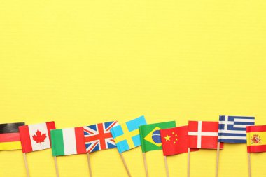 Sarı arka planda farklı ülkelerin küçük kağıt bayrakları, düz. Metin için boşluk