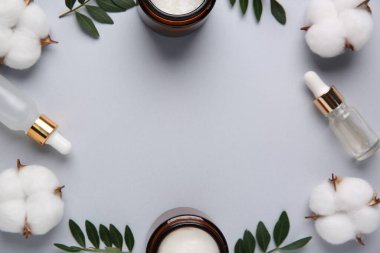 Farklı kozmetik ürünleri, gri arka planda yapraklar ve pamuk çiçekleri, düz bir zemin. Metin için boşluk