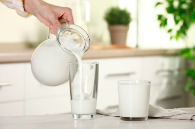 Mutfaktaki hafif ahşap masada, sürahiden bardağa taze süt döken kadın, yakın plan.