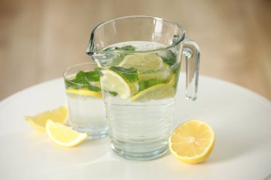 Sürahi içinde nane ve beyaz masada cam ile limonata tazeleniyor.