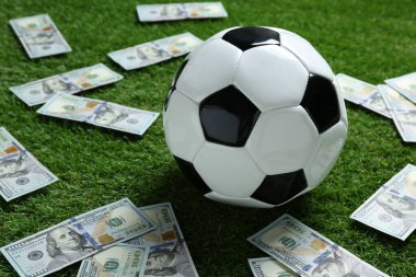 Yeşil çimlerin üzerinde futbol topu ve dolar banknotları