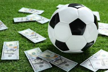Yeşil çimlerin üzerinde futbol topu ve dolar banknotları