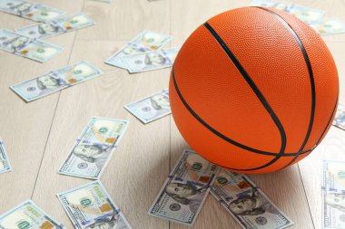 Basketbol topu ve dolar banknotları ahşap masada.