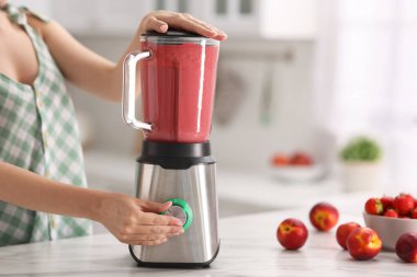 Mutfaktaki beyaz mermer masada blender ile nefis smoothie yapan kadın, yakın plan.