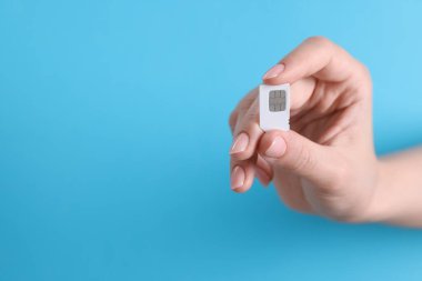 Açık mavi arka planda SIM kartı tutan kadın, yakın plan. Metin için boşluk