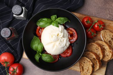 Lezzetli burrata peyniri, domates, fesleğen ve ekmek kahverengi masada, düz yatıyordu.
