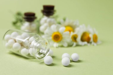 Yeşil arka planda homeopatik ilaç ve papatya çayı şişeleri, yakın plan.