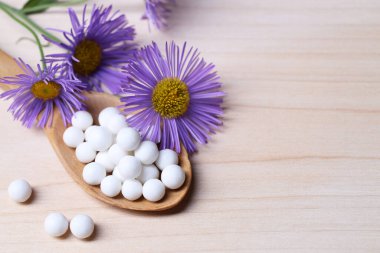 Homeopati. Haplı kaşık ve ahşap masada yabani çiçekler, metin için yer.