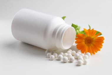 Homeopatik tedavi. Beyaz arka planda bir sürü hap ve takvim çiçeği olan bir şişe.